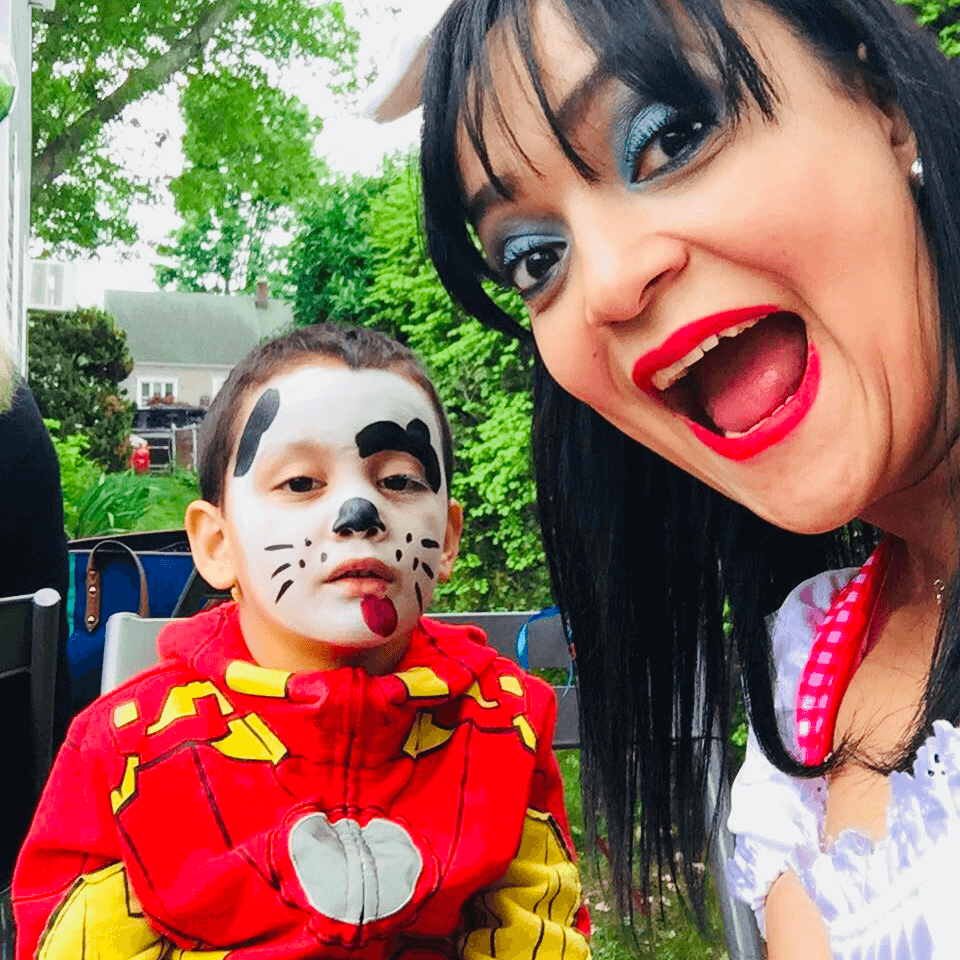 Niño con maquillaje facial de perrito y disfraz de superhéroe, junto a animadora con orejas de conejo en una fiesta infantil al aire libre.