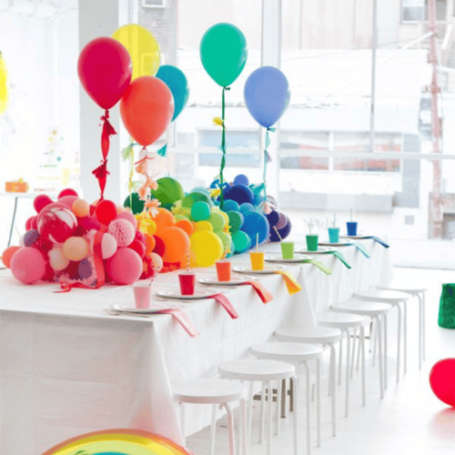 A table decorated with birthday theme on which there are many balloons of different colors, birthday plates and glasses, is a party decoration offered by Fabiola's Kids.